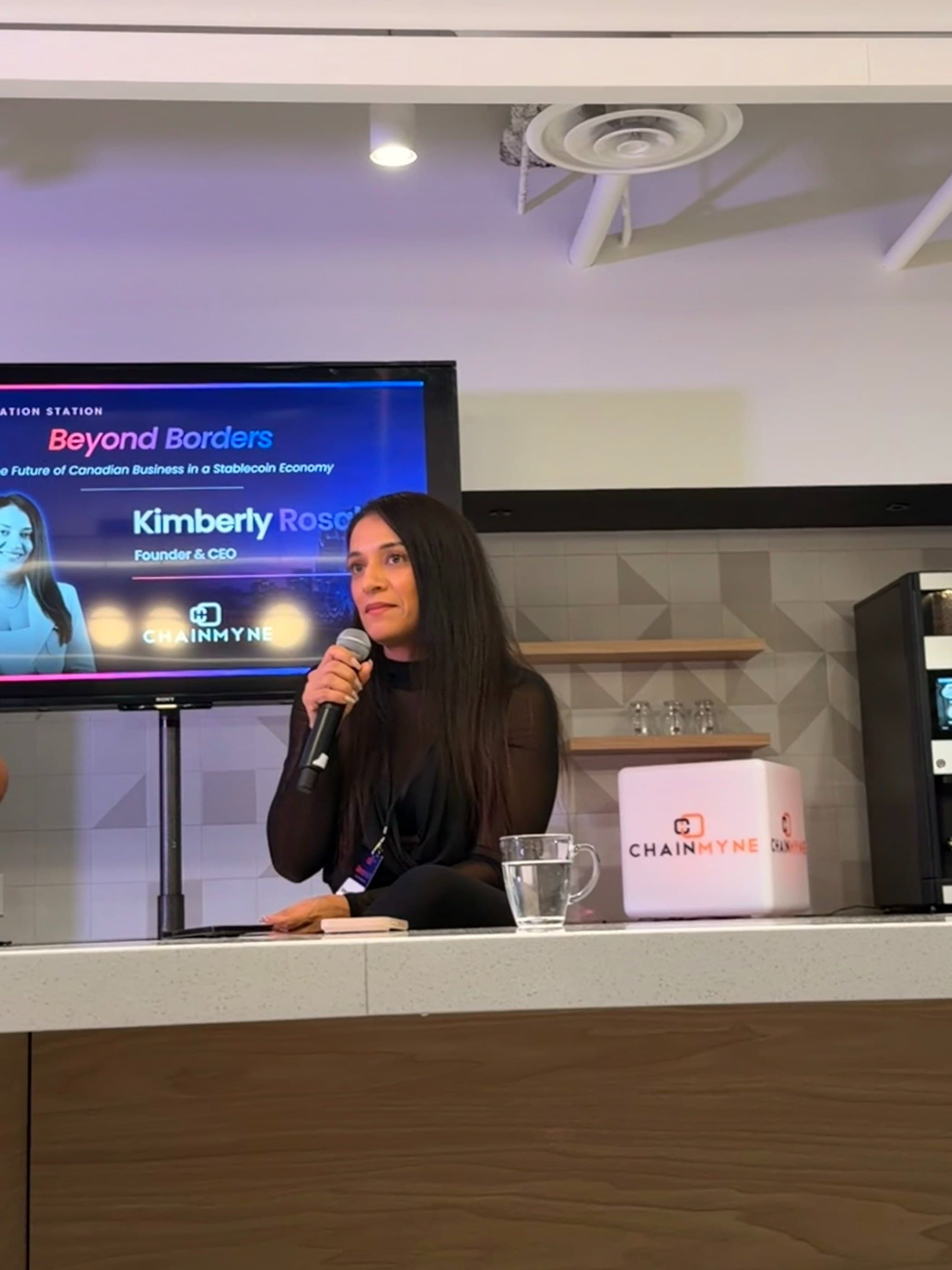Kimberly Rosales speaking into a microphone at a Beyond Borders session, her name on the screen behind her