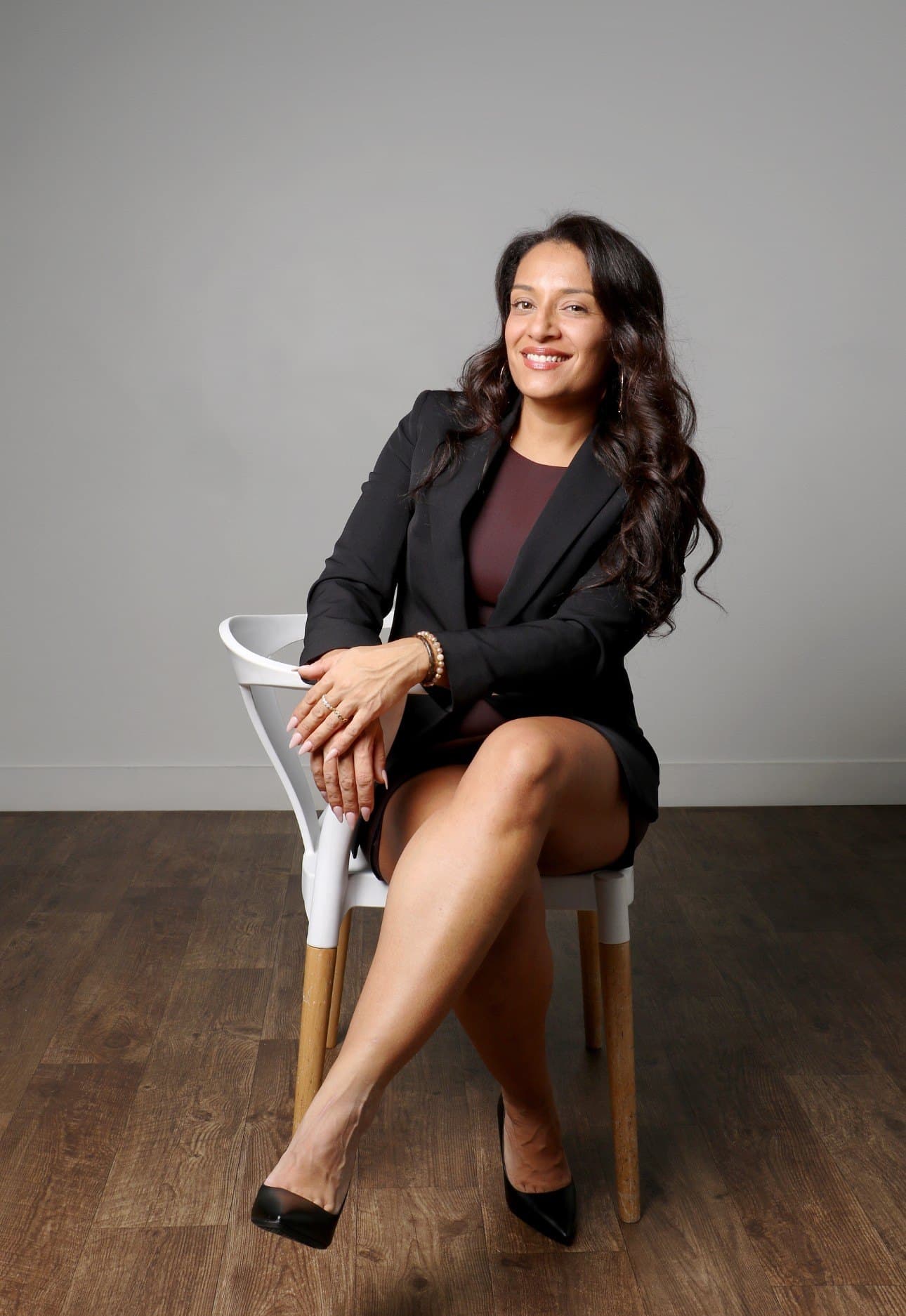 Kimberly Rosales seated on a white chair in a black blazer, smiling